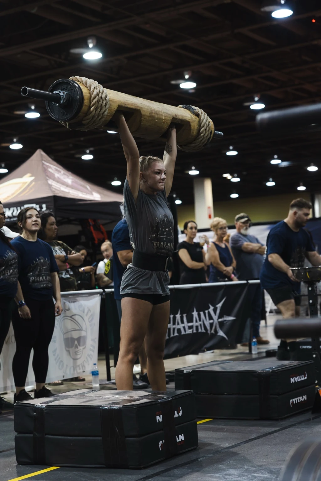 Strongwoman athlete holding a log overhead during competition